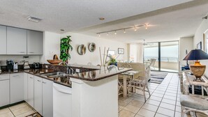 A modern kitchen with white cabinets, a granite countertop, and a dining area with wicker furniture. - Gulf Front Condo with Stunning Views! (Pensacola)