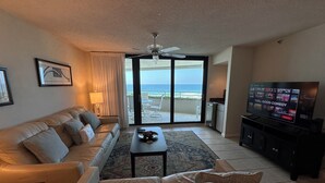 A living room with a sofa, a coffee table, a television, and a view of the ocean through a sliding door. - Gulf Front Condo with Stunning Views! (Pensacola)