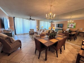 A spacious living room with a dining area, large windows, and a ceiling fan.