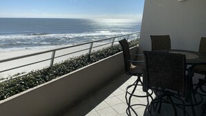A balcony with a view of the ocean, a table with chairs, and a railing. - Gulf Front Condo with Stunning Views! (Pensacola)