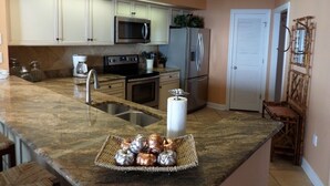 A kitchen with granite countertops, stainless steel appliances, and a central island with a basket of decorative items. - Gulf Front Condo with Stunning Views! (Pensacola)