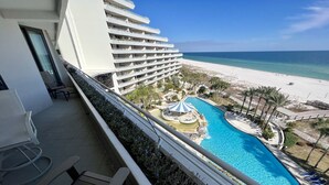 Ein Hotelbalkon mit Pool, Strandblick und Liegestühlen.