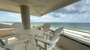 Ein überdachter Sitzbereich im Freien mit weißen Stühlen und einem Tisch, mit Blick auf einen Strand und einen klaren Meerblick.