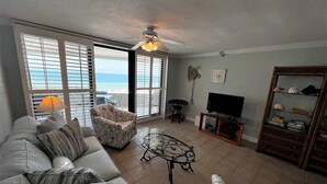 A living room with a sofa, armchairs, a coffee table, a TV, and a bookshelf. - Gulf Front Condo with Stunning Views! (Pensacola)
