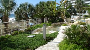 A landscaped garden with a stone pathway, palm trees, and a water feature. - Gulf Front Condo with Stunning Views! (Pensacola)
