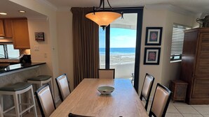 A dining area with a large table, chairs, a bowl, a pendant light, and a view of the ocean through a window. - Gulf Front Condo with Stunning Views! (Pensacola)