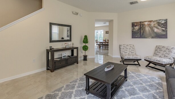A spacious living room with a dark wooden coffee table, two patterned armchairs, a dark console table, and a large mirror. A framed painting adorns the wall, and a potted plant adds greenery. - Renewed luxury property 20 min from Disney and major parks (Davenport)