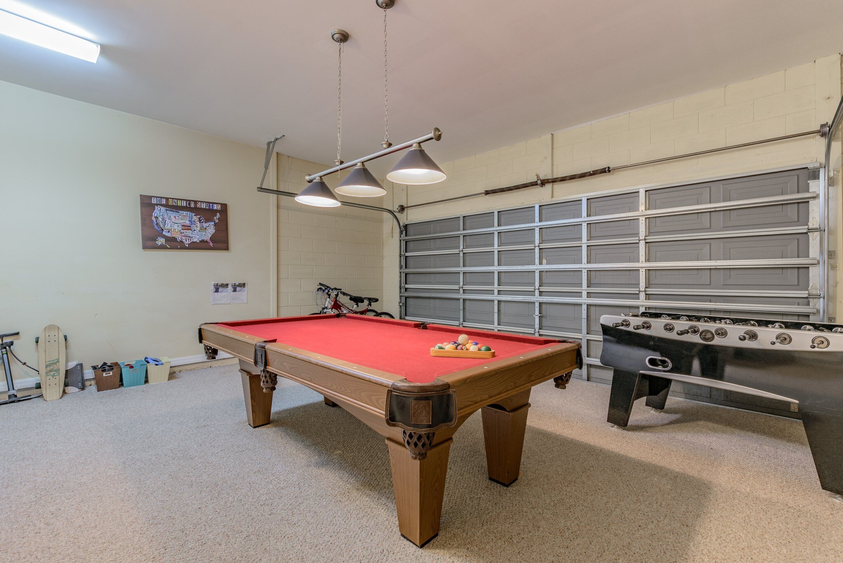Une table de billard recouverte d’un drap de feutre rouge, une table de baby-foot et un vélo à l’arrière-plan.