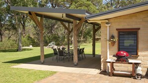 Un patio techado con mesa y sillas, una parrilla de barbacoa y un edificio de ladrillo al fondo.
