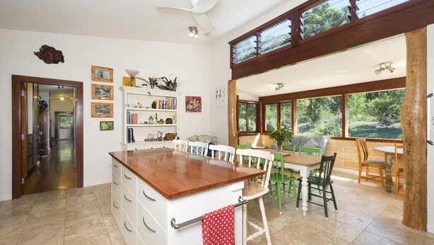 Una cocina amplia con una isla de madera, un comedor con sillas verdes y ventanas grandes que ofrecen vistas al exterior.