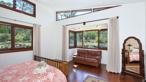 Un dormitorio con una cama grande, un sofá de cuero marrón y múltiples ventanas que ofrecen vistas a un paisaje natural.