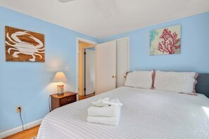 Un dormitorio con cama, mesita de noche, lámpara y dos cuadros.