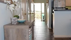 A hallway with wooden flooring, a kitchen area with a refrigerator, and a door leading to a balcony.