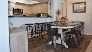 A modern kitchen with wooden cabinets, a microwave, and a dining area with a round table and metal chairs.