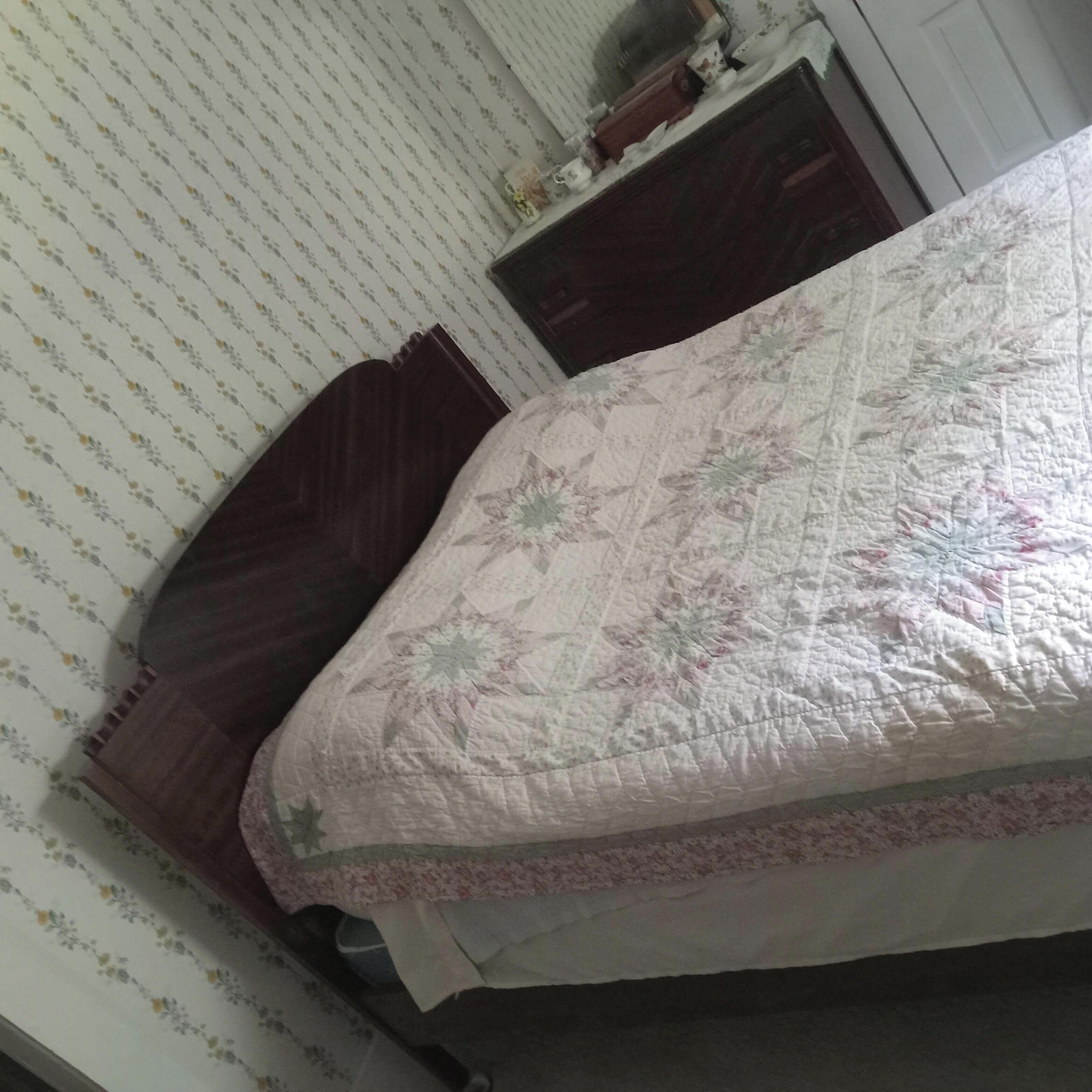 Een slaapkamer met een bed, een houten nachtkastje, een dressoir en behang met een patroon.