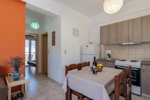 Una cocina compacta con una mesa de comedor, sillas, un refrigerador, estufa y un florero con flores sobre una mesita auxiliar.
