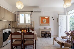Una cocina con armarios de madera, una mesa de comedor con sillas, un ventanal con cortinas y un equipo de aire acondicionado.