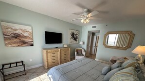 A bedroom with a bed, a TV, a ceiling fan, and artwork on the walls. - Gulf Front Condo with Stunning Views! (Pensacola)