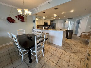 A modern kitchen with white cabinetry, a central island, and a dining area with a black table and white chairs.