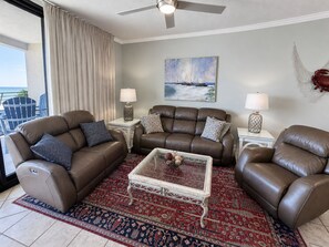 A living room with a brown leather sofa set, a glass coffee table, and a patterned rug.
