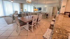 A spacious living area with a dining table, chairs, and a kitchen counter. - Gulf Front Condo with Stunning Views! (Pensacola)