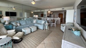 A spacious living room with a sectional sofa, a dining area, and a kitchen in the background. - Gulf Front Condo with Stunning Views! (Pensacola)