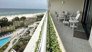 A balcony with a view of the beach, lounge chairs, and a pool. - Gulf Front Condo with Stunning Views! (Pensacola)