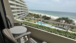 A balcony with two Adirondack chairs, a pool, and a view of the beach and ocean. - Gulf Front Condo with Stunning Views! (Pensacola)