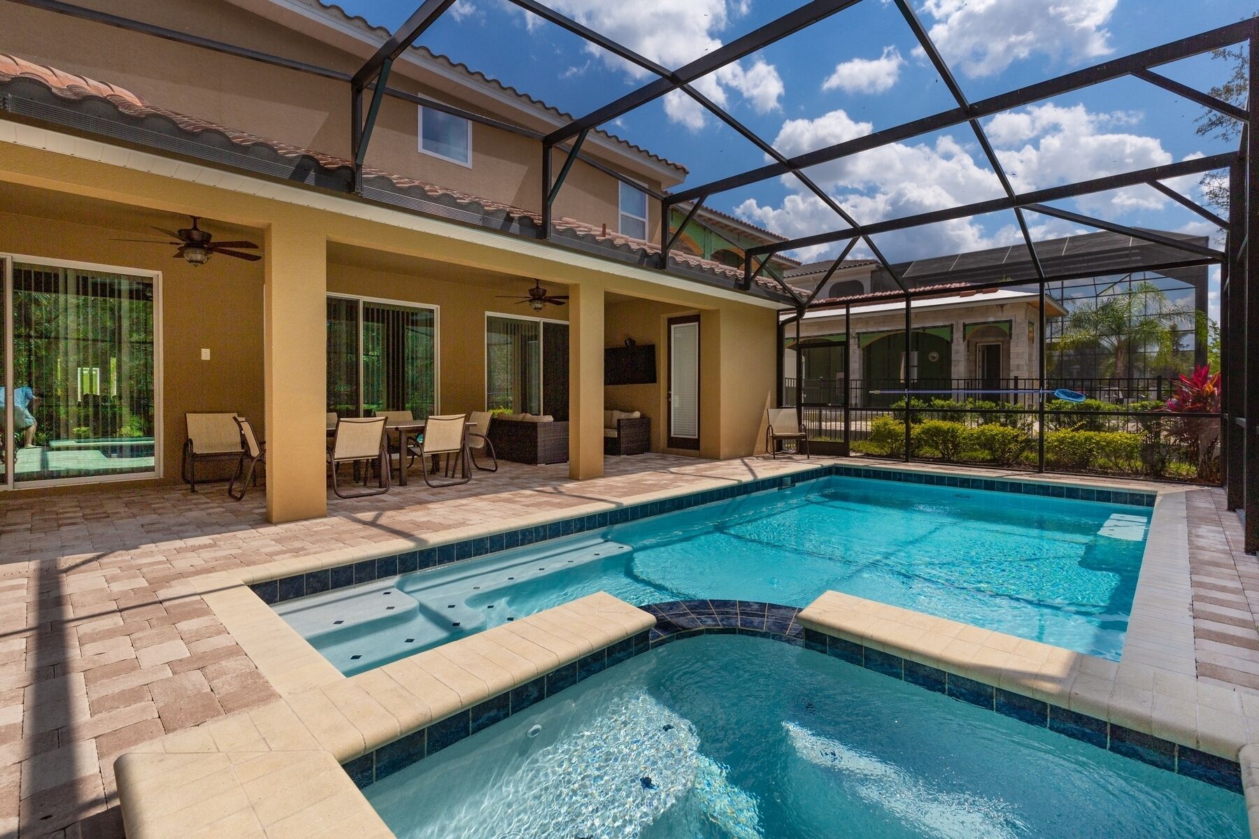 Piscina con cerramiento de vidrio, mobiliario de patio y ventilador de techo.