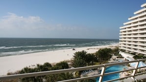 Uitzicht op het strand vanaf een hotelbalkon, met een zwembad en palmbomen.