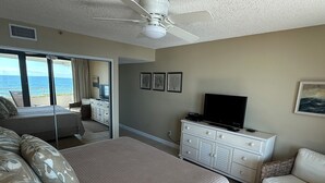 Een slaapkamer met een bed, een televisie op een dressoir en uitzicht op de oceaan door een schuifdeur.