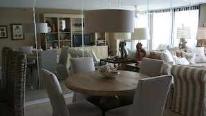 Een moderne woonkamer met een ronde houten tafel, comfortabele fauteuils, een grote lamp en een boekenkast op de achtergrond.