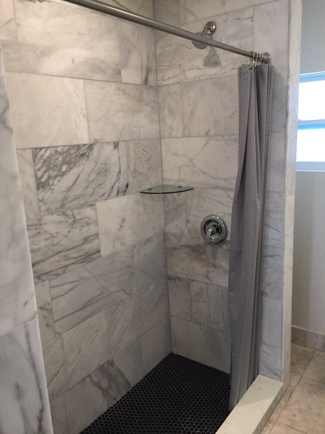 Une douche à l’italienne avec des murs en marbre, une étagère en verre et un rideau de douche.