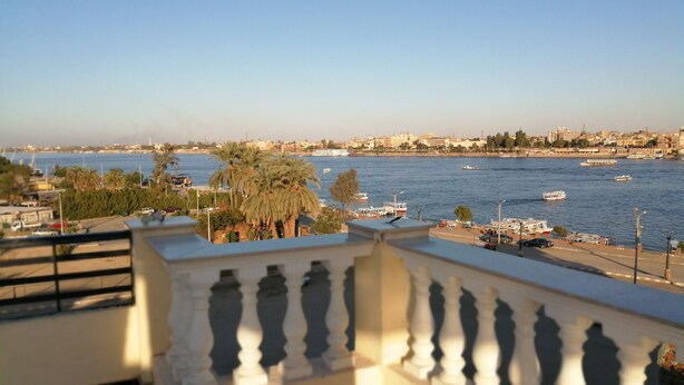 A balcony with a railing overlooking a waterfront with boats and buildings in the background. - Nile Jewel Suites Luxor Egypt , Luxury fully Serviced Nile View Apartment  (Qurna)