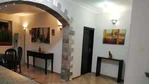 A dining area with a table and chairs, a stone pillar, and artwork on the walls. - Nile Jewel Suites Luxor Egypt , Luxury fully Serviced Nile View Apartment  (Qurna)