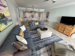 Uma sala de estar com sofá seccional, um banquinho e uma televisão sobre um armário de madeira.