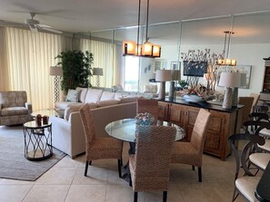 A modern living room with a round glass table, wicker chairs, a sofa, and a dining area with a wooden cabinet.