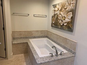 A bathroom with a freestanding bathtub, granite countertops, a wall-mounted towel rack, and a floral painting. - Gulf Front Condo with Stunning Views! (Pensacola)