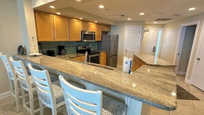 A modern kitchen with granite countertops, stainless steel appliances, and light blue chairs. - Gulf Front Condo with Stunning Views! (Pensacola)