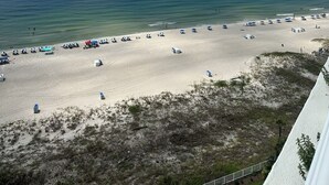 A beach with clear skies, calm waters, and several beach umbrellas and tents. - Gulf Front Condo with Stunning Views! (Pensacola)