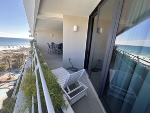 A balcony with a pool, chairs, and a table overlooking the beach.