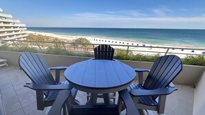 A balcony with a round table and four Adirondack chairs, overlooking a beach with a clear view of the ocean. - Gulf Front Condo with Stunning Views! (Pensacola)