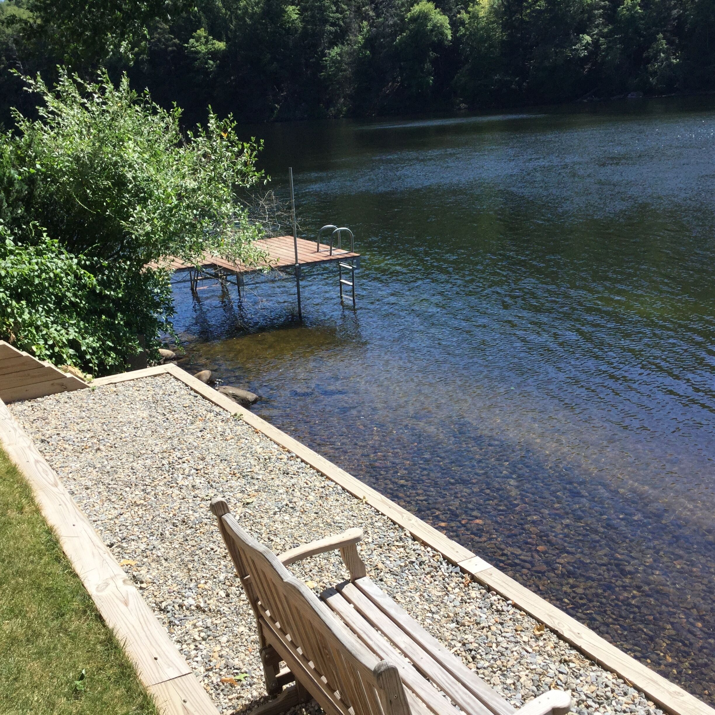A wooden dock extending into a lake, surrounded by trees and pebbles.