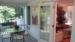 Eine überdachte Veranda mit einem Glastisch und Stühlen, einem Kamin aus Ziegelsteinen und Blick auf den Garten.