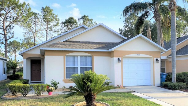 A single-story house with a front garage, a small front yard with a palm tree, and a mailbox. - SOUTHERN DUNES VILLA - GOLF! POOL! CLOSE TO DISNEY, LEGOLAND, UNIVERSAL! (Haines City)
