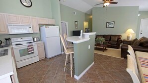 A compact kitchen with a microwave, stove, and refrigerator. There is a dining area with a table and chairs. - SOUTHERN DUNES VILLA - GOLF! POOL! CLOSE TO DISNEY, LEGOLAND, UNIVERSAL! (Haines City)