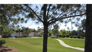 A residential lawn with a curved driveway, surrounded by trees and houses. - SOUTHERN DUNES VILLA - GOLF! POOL! CLOSE TO DISNEY, LEGOLAND, UNIVERSAL! (Haines City)