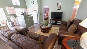 A living room with a brown leather sofa, a coffee table with a plant, and a TV. - SOUTHERN DUNES VILLA - GOLF! POOL! CLOSE TO DISNEY, LEGOLAND, UNIVERSAL! (Haines City)