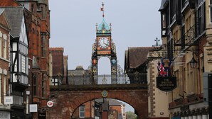 Ein historischer Glockenturm mit einer Brücke im Hintergrund.