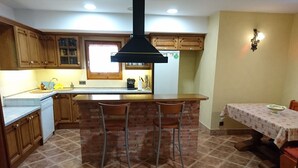 A kitchen with a central island, wooden cabinets, a built-in oven, and a dining area with a table and chairs. - Charming house located in the Espinalbet area. (Castellar del Riu)